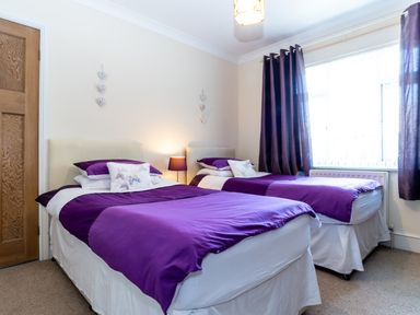 A bedroom with two single beds with purple bedding and a bedside lamp at Tomeg in Amble-by-the-Sea