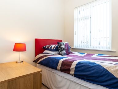 A bedroom with a single bed with union jack bedding a red headboard a wooden bedside table and a red lamp at Tomeg in Amble-by-the-Sea