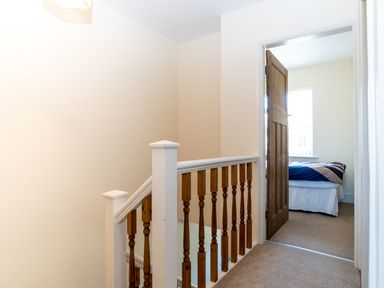 A hallway with wooden staircase railing and an open door leading to a bedroom with a bed at Tomeg in Amble-by-the-Sea