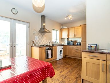 A kitchen with wooden cabinets a washing machine oven microwave and a table with a red polka dot tablecloth at Tomeg in Amble-by-the-Sea