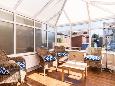 A sunroom with wicker chairs and blue cushions around a wooden table at Tomeg in Amble-by-the-Sea