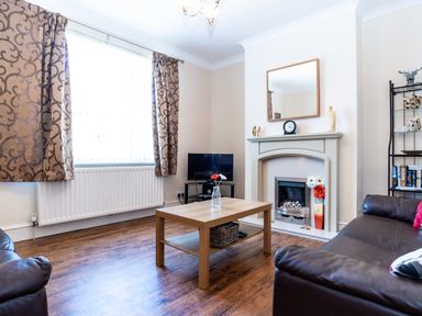 A living room with brown leather sofas a wooden coffee table a flat screen television and a fireplace at Tomeg in Amble-by-the-Sea