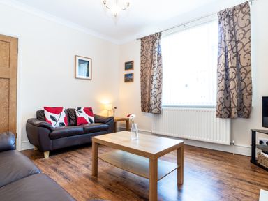 A living room with leather sofas a wooden coffee table a lamp and patterned curtains at Tomeg in Amble-by-the-Sea