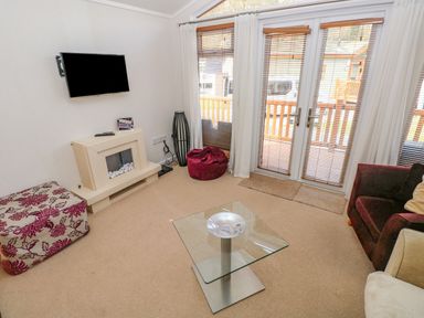 A living room with a wall-mounted TV a glass coffee table and doors leading to a balcony at Cladebrine Wisemans Bridge near Saundersfoot