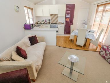 A living room with a sofa pillows glass coffee table and an open kitchen and dining area at Cladebrine Wisemans Bridge near Saundersfoot
