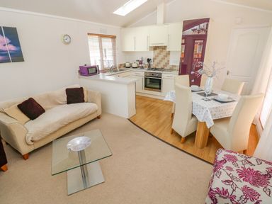 A living room with a sofa a glass coffee table and a dining table next to a kitchen at Cladebrine Wisemans Bridge near Saundersfoot