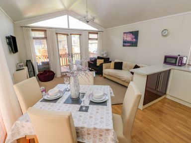 An open living and dining area with a table set for four chairs two sofas and kitchen cabinets at Cladebrine Wisemans Bridge near Saundersfoot
