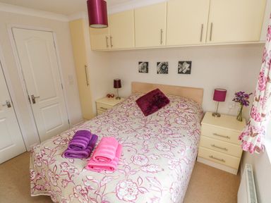 A bedroom with a bed covered in floral bedding towels on the bed and cabinets above the bed at Cladebrine in Wisemans Bridge near Saundersfoot