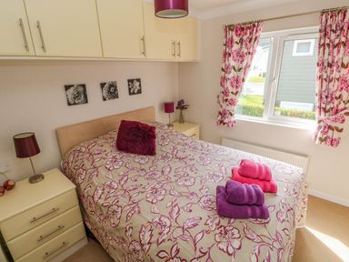 A bedroom with a double bed with floral bedding and folded towels beside a window at Cladebrine Wisemans Bridge near Saundersfoot
