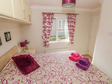 A bedroom with a bed covered in floral bedding purple and pink towels on bed floral curtains at Cladebrine Wisemans Bridge near Saundersfoot