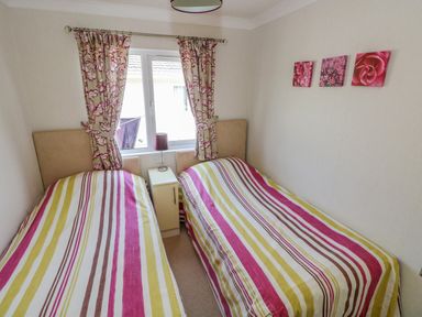 A bedroom with two single beds side by side striped bedding a window with floral curtains and three floral pictures on the wall at Cladebrine in Wisemans Bridge near Saundersfoot