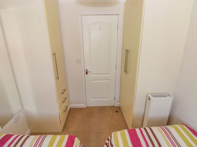 A bedroom with two striped beds a white door between two closets and a radiator at Cladebrine Wisemans Bridge near Saundersfoot