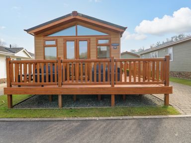 A wooden cabin with a front deck with railings and outdoor seating at Cladebrine Wisemans Bridge near Saundersfoot