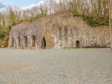 An outdoor area with an old stone wall featuring multiple arched openings and surrounded by trees at Cladebrine Wisemans Bridge near Saundersfoot