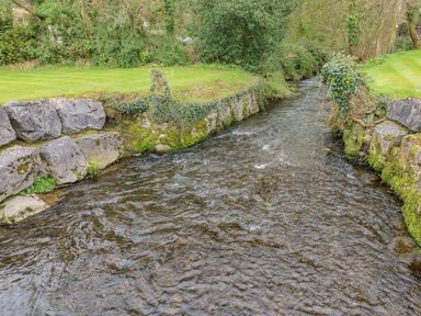 A narrow stream flowing between grassy banks with stone walls covered in moss and ivy at Cladebrine Wisemans Bridge near Saundersfoot