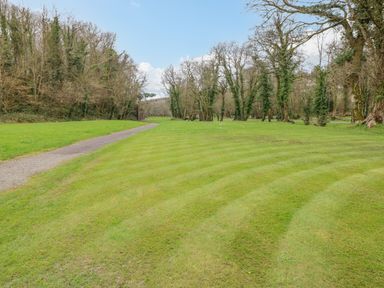 A grassy field with a paved pathway and trees in the background at Cladebrine Wisemans Bridge near Saundersfoot
