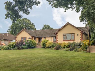 A single story house with a garden and lawn in front surrounded by trees at Pipistrelle Lodge in Plymtree