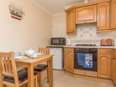 A kitchen with wooden cabinets a small dining table with two chairs a microwave oven and a toaster at Pipistrelle Lodge in Plymtree
