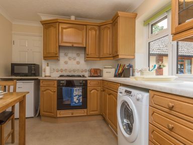 A kitchen with wooden cabinets stove washing machine microwave and countertop at Pipistrelle Lodge in Plymtree