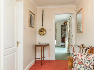 A hallway with a small wooden table and a wall-mounted brass pan next to an open door showing another room at Pipistrelle Lodge in Plymtree