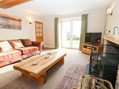 A living room with a wooden coffee table a red patterned sofa a wooden TV stand with a TV and a fireplace with firewood at Ty Top in Llanfaethlu