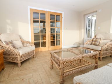 A living room with rattan furniture and a glass coffee table at Ty Top in Llanfaethlu