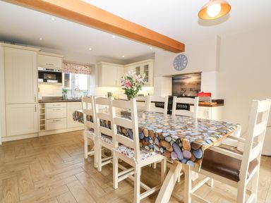 A kitchen with a dining table covered by a pebble-patterned tablecloth and white chairs at Ty Top in Llanfaethlu