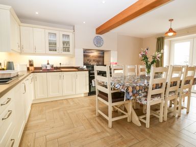 A kitchen with cream cabinets wooden floor dining table with floral and patterned chairs and flowers in a vase at Ty Top in Llanfaethlu