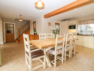 A kitchen with a wooden dining table and chairs and cabinets and a staircase in the background at Ty Top in Llanfaethlu