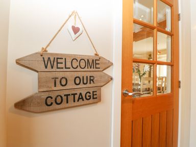 A wooden sign saying welcome to our cottage hanging on a wall next to a wooden door with glass panels at Ty Top in Llanfaethlu