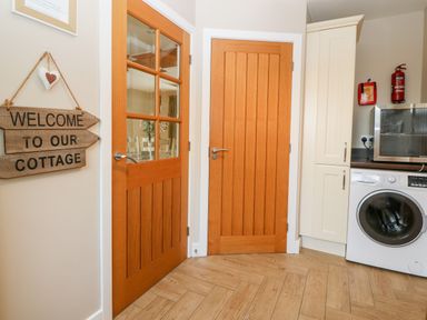 A kitchen area with wooden doors a washing machine a microwave and a welcome sign at Ty Top in Llanfaethlu