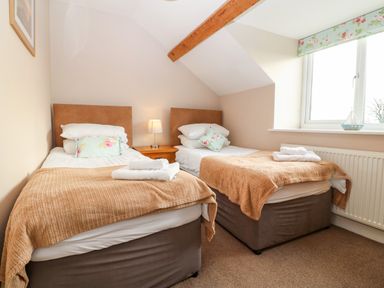 A bedroom with two single beds bedside table with lamp and a window at Ty Top in Llanfaethlu