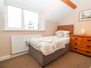 A bedroom with a single bed beside a window and a wooden dresser with a lamp at Ty Top in Llanfaethlu