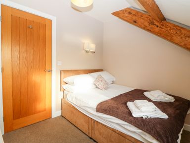 A bedroom with a bed with pillows and towels folded on it near a wooden door with a wall light and exposed wooden ceiling beams at Ty Top in Llanfaethlu