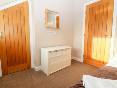 A bedroom corner with two wooden doors a white chest of drawers and a wall mirror at Ty Top in Llanfaethlu