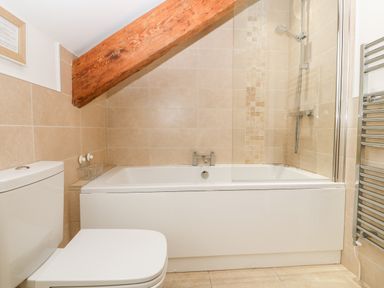 A bathroom with a bathtub shower toilet and a wooden beam at Ty Top in Llanfaethlu