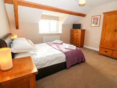 A bedroom with a double bed a wooden dresser wardrobe and a bedside table with lamps at Ty Top in Llanfaethlu