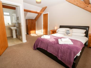 A bedroom with a bed a purple blanket towels wooden furniture and an ensuite bathroom at Ty Top in Llanfaethlu