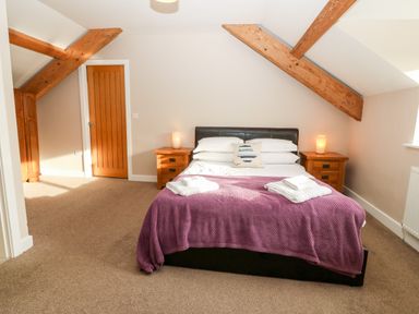 A bedroom with a double bed covered by a purple blanket two wooden bedside tables with lamps and folded towels on the bed at Ty Top in Llanfaethlu