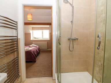 A bathroom with a shower stall and a door leading to a bedroom with a bed covered by a purple blanket at Ty Top in Llanfaethlu