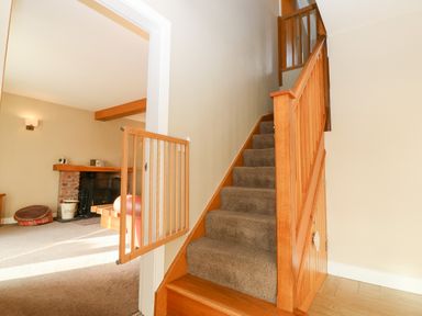 A carpeted staircase with wooden railing and baby gate next to a living room with fireplace and pet bed at Ty Top in Llanfaethlu
