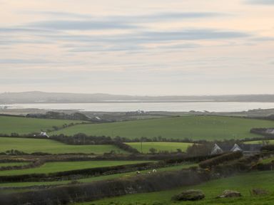 Green fields with sheep and scattered houses near a body of water at Ty Top in Llanfaethlu