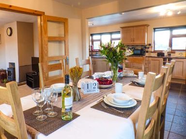 A dining table set with plates glasses wine bottle and flowers in a kitchen at Tynddol Bungalow Llanbadarn-Fynydd near Llanbister