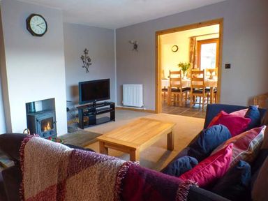 A living room with a wooden coffee table a television a fireplace and a sofa with cushions next to a dining room at Tynddol Bungalow in Llanbadarn-Fynydd near Llanbister