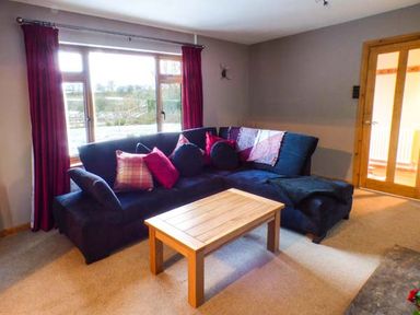 A living room with a dark blue sectional sofa with cushions and a wooden coffee table near a large window at Tynddol Bungalow in Llanbadarn-Fynydd near Llanbister