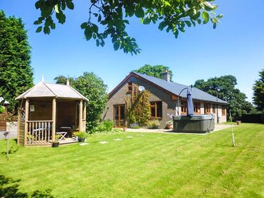 A bungalow with a wooden gazebo and inflatable hot tub in a garden at Tynddol Bungalow in Llanbadarn-Fynydd near Llanbister