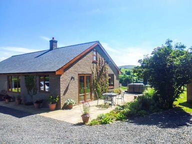 A bungalow with a patio table and chairs and potted plants outside at Tynddol Bungalow in Llanbadarn-Fynydd near Llanbister