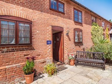 Exterior of a brick cottage with a wooden door, windows, potted plants and a wooden bench at Punch Cottage Little Glemham near Wickham Market