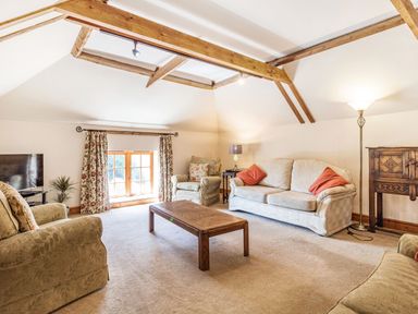 A living room with sofas armchairs a coffee table a TV a window with floral curtains and wooden ceiling beams at Punch Cottage in Little Glemham near Wickham Market