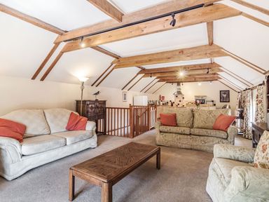 A living room with sofas a wooden coffee table exposed ceiling beams and an open kitchen at Punch Cottage in Little Glemham near Wickham Market